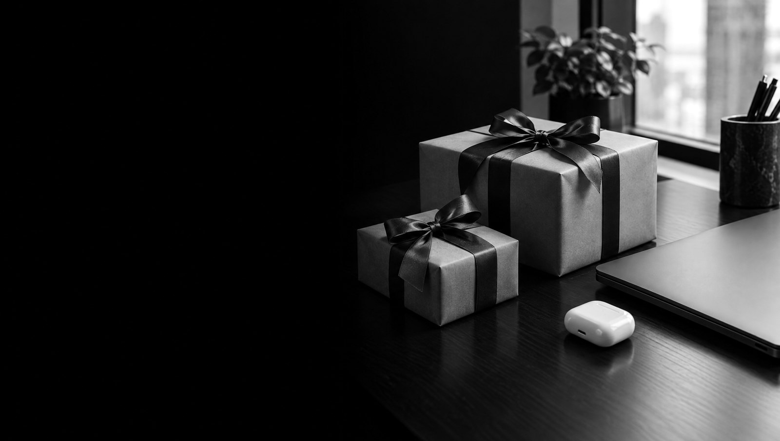 Paquets cadeaux à côté d'un PC portable sur un bureau, photo noir et blanc